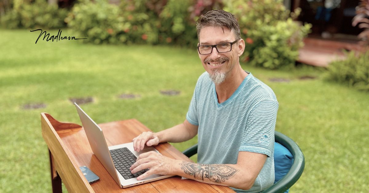 Madhava sitzt mit Laptop am Schreibtisch