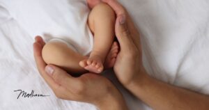 2 erwachsene Hände halten die Beine eines Babys