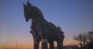 Großes hölzernes trojanisches Pferd vor einem Abendhimmel, der von Blau in Orange übergeht, Sinnbild für eine gut gemeinte Gabe, die man nicht ablehnen darf