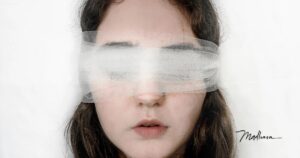 Junge Frau mit langen braunen Haaren, die Augen mit einem durchscheinenden weißen Tüllband verbunden, die Lippen leicht geöffnet, vor weißem Hintergrund, Sinnbild für verordnetes Vertrauen und aufgegebene Wahrnehmung.